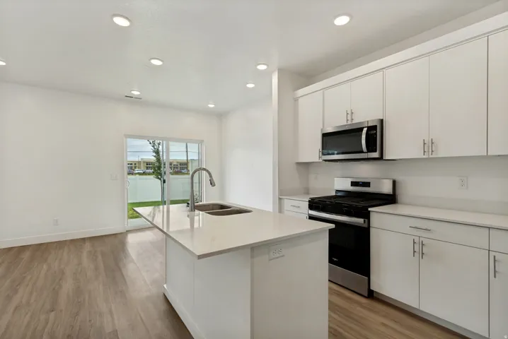 Modern kitchen featuring an quartz island with a double basin sink, white cabinetry, integrated stainless steel microwave, gas range, and laminate flooring