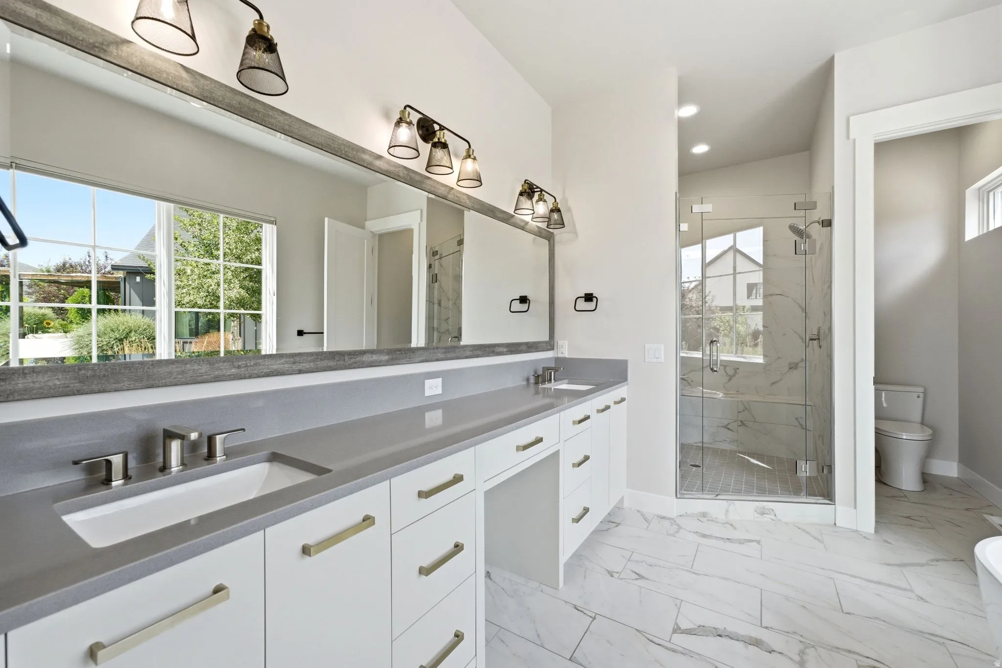 Bathroom featuring an extended double vanity with undermount sinks, gray countertops, and white cabinetry with gold-tone hardware