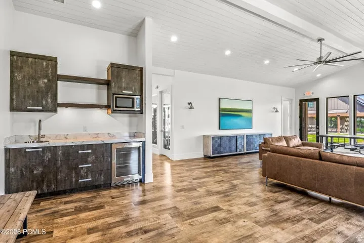 Spacious common area featuring wood-finish flooring, a vaulted ceiling with exposed beams, and a built-in wet bar with a microwave and beverage cooler