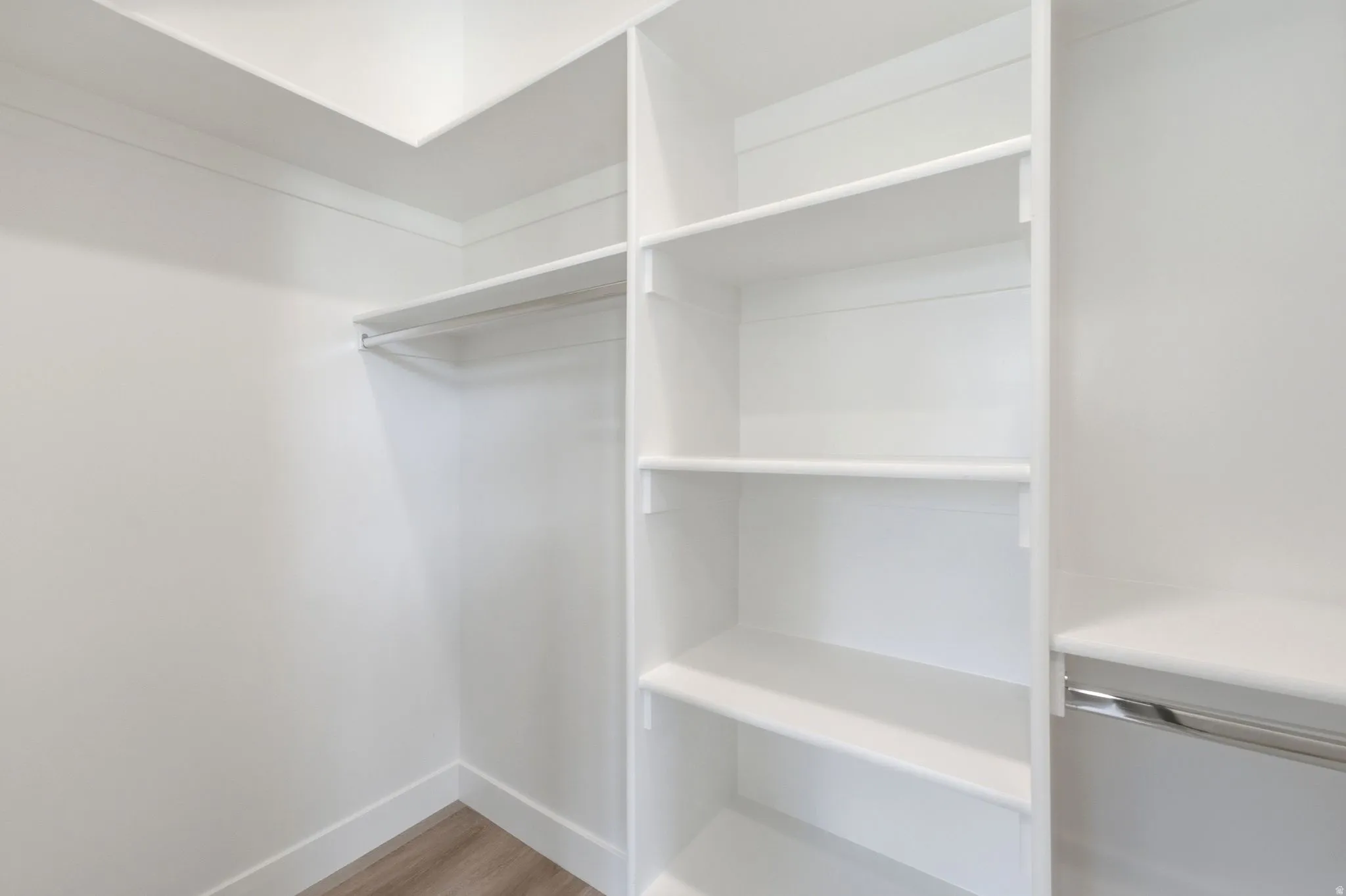Walk-in closet featuring white built-in shelving, white walls, and wood-finish flooring