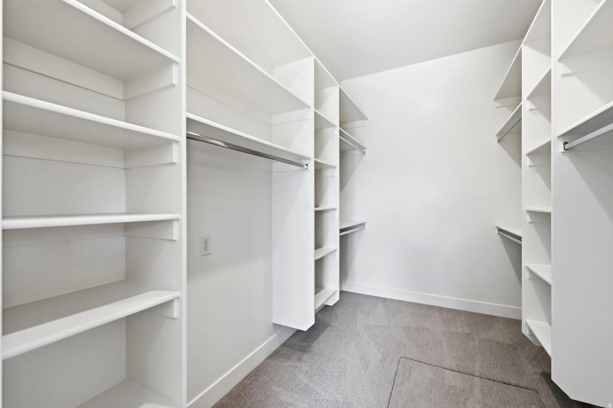 Walk-in closet featuring white built-in shelving, multiple hanging rods, and grey carpet flooring
