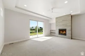 Spacious room featuring a stone-clad fireplace, built-in shelving, tray ceiling, recessed lighting, and sliding glass doors opening to outdoor green space