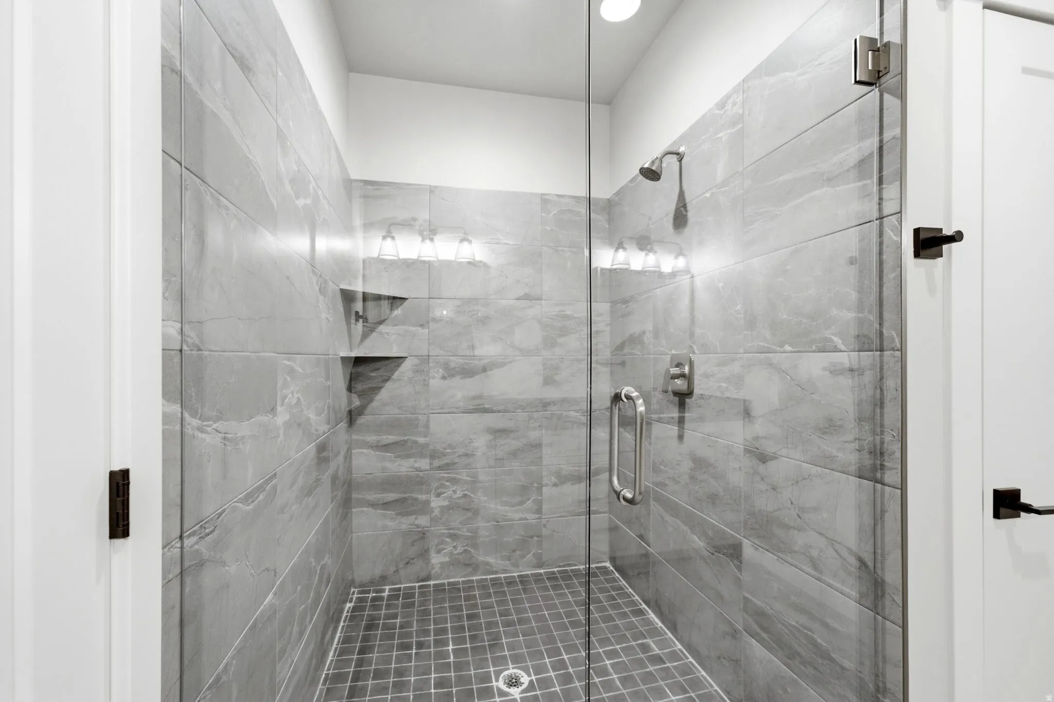 Glass-enclosed shower featuring large format gray tile walls and a mosaic tile floor