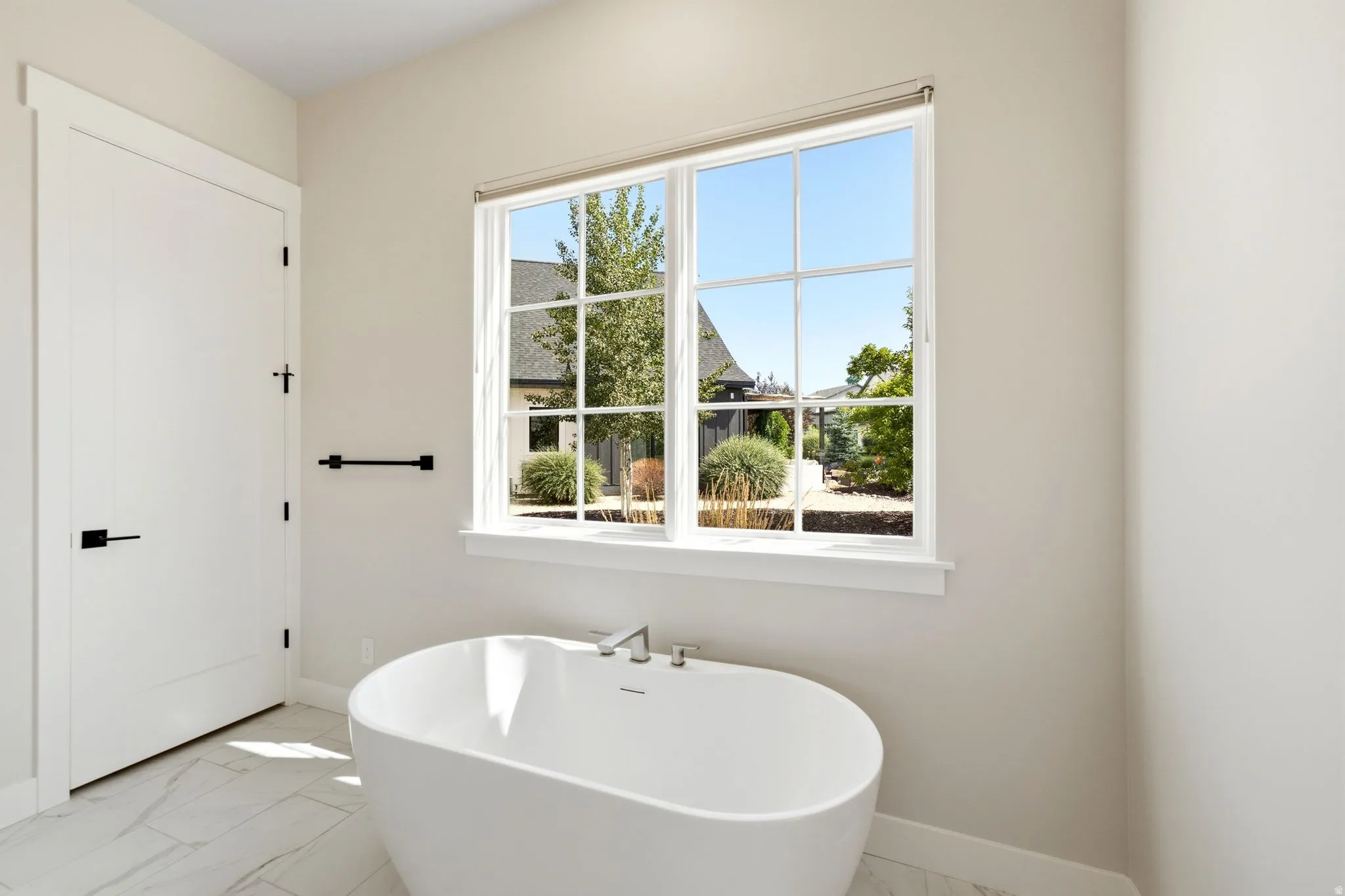 Freestanding soaking tub with a modern faucet set below a large grid-pane window