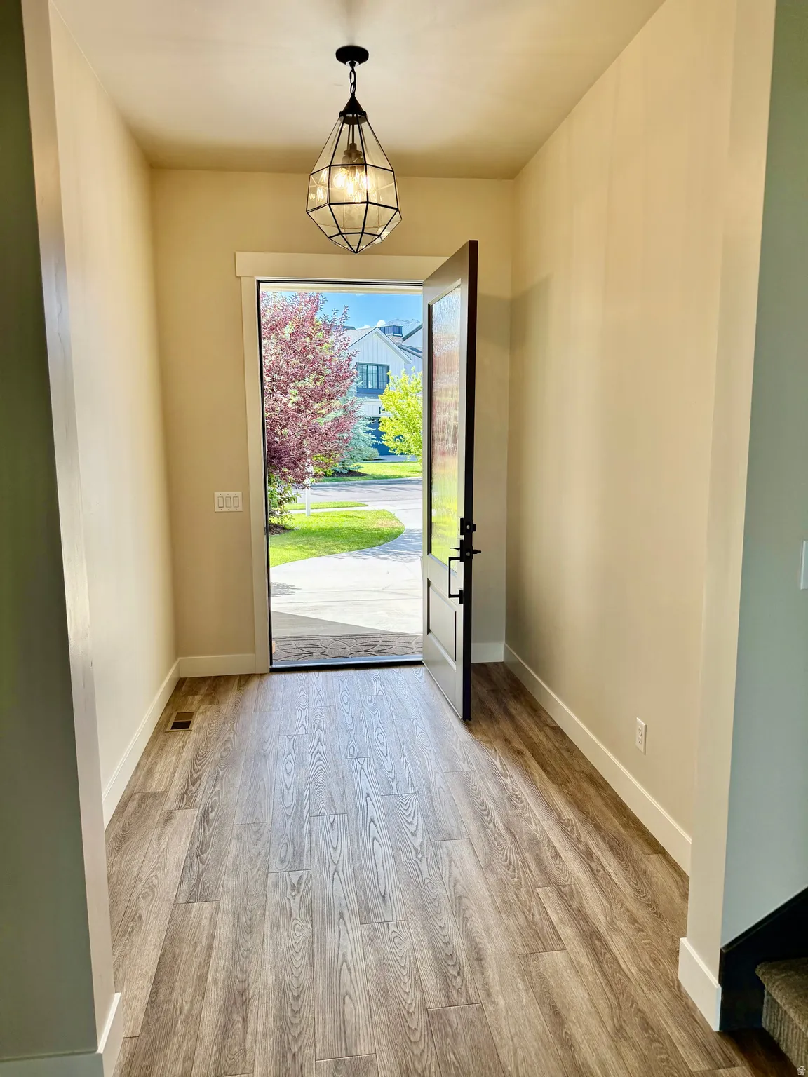 Inviting entryway featuring wood-finish flooring, a geometric pendant light fixture, and a dark-paneled front door with matte black hardware