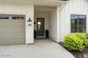 Modern farmhouse exterior featuring vertical white siding, a recessed entry, a glass-paneled front door, an attached garage with window inserts, and mature landscaping