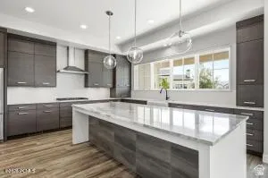 Gourmet kitchen featuring a large central island with a stone countertop, dark wood-finish cabinetry, stainless steel appliances, pendant lighting, and wood-finish flooring