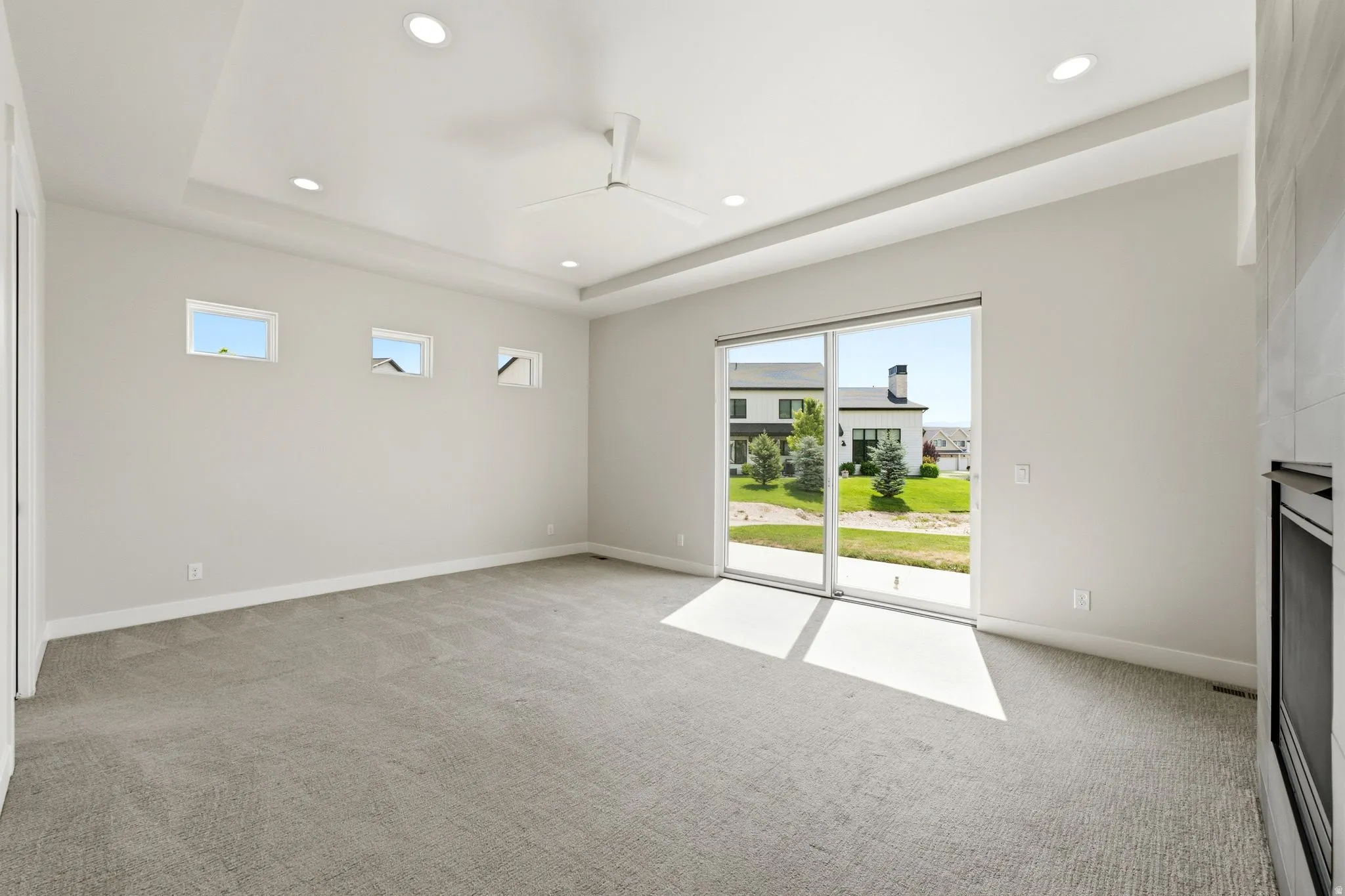 Spacious room featuring a tray ceiling with recessed lighting, a ceiling fan, and light gray wall-to-wall carpeting