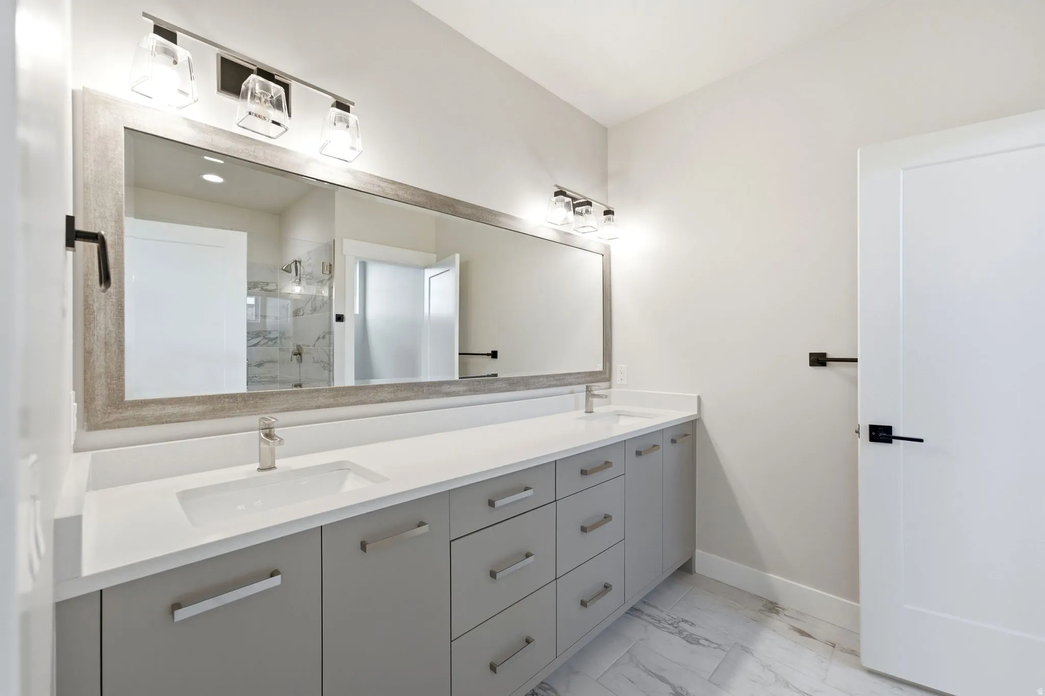 Double vanity with integrated sinks, white countertops, gray cabinetry, brushed nickel hardware, and wood-finish framed mirror