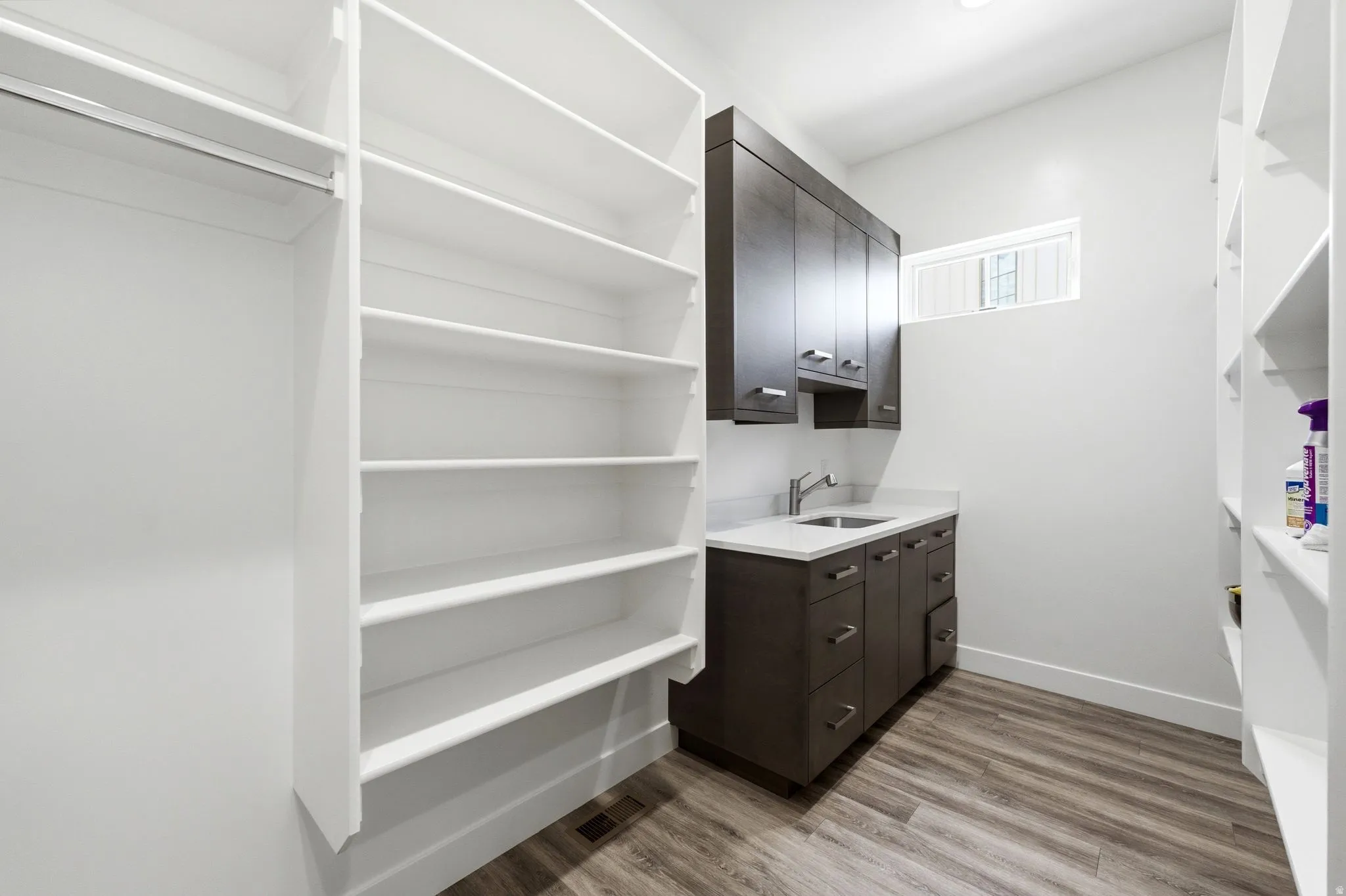 Dedicated utility room featuring extensive built-in shelving, dark wood-finish cabinetry, a utility sink with a chrome faucet, and wood-finish flooring