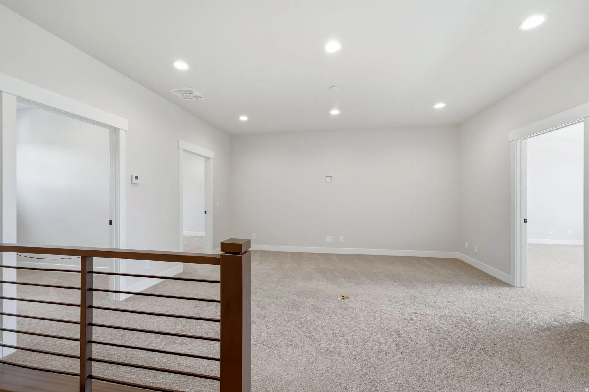 Open landing area featuring light-toned carpet, recessed ceiling lighting, and a modern wood-finish railing with horizontal balusters