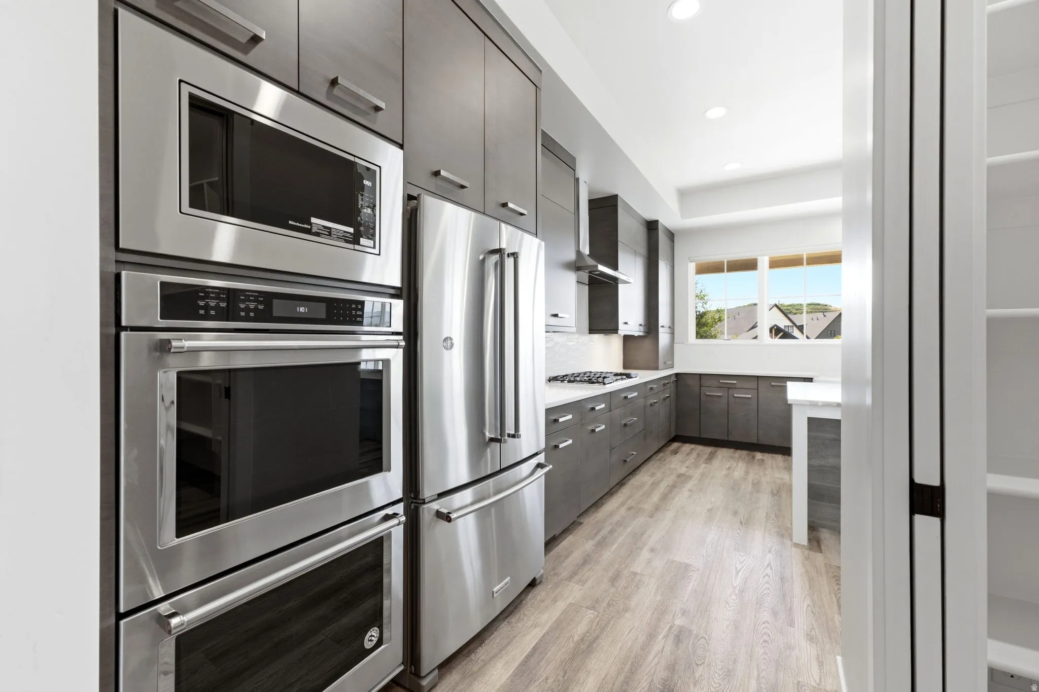 Modern kitchen featuring stainless steel appliances, dark wood-finish cabinetry, light wood-finish flooring, white countertops, and recessed lighting
