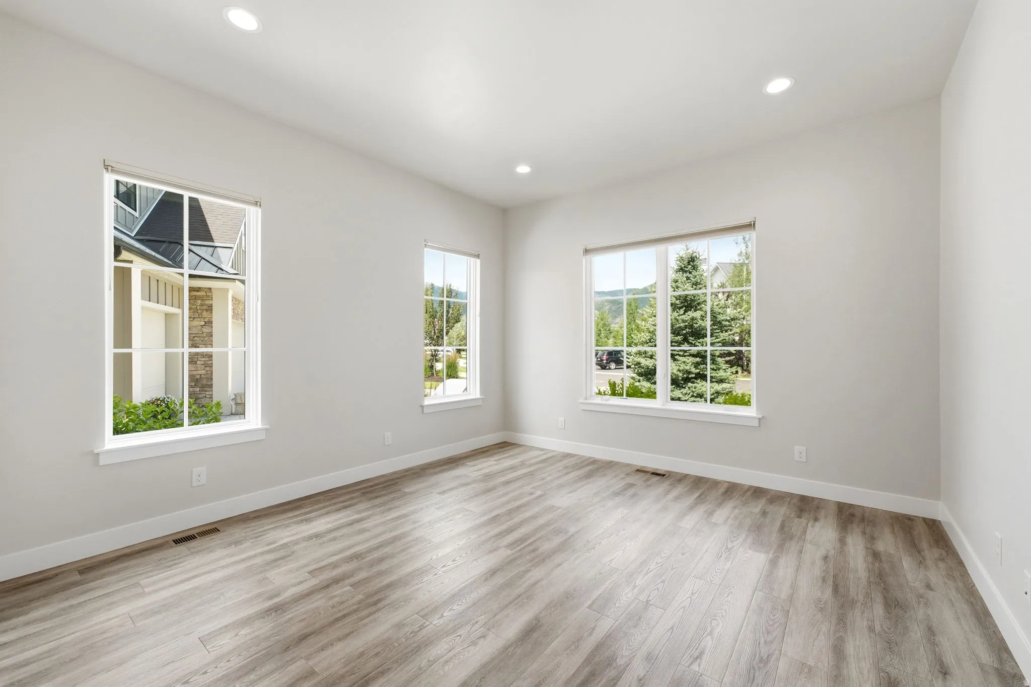 Spacious room featuring light wood-finish flooring, recessed lighting, and multiple large windows with white trim
