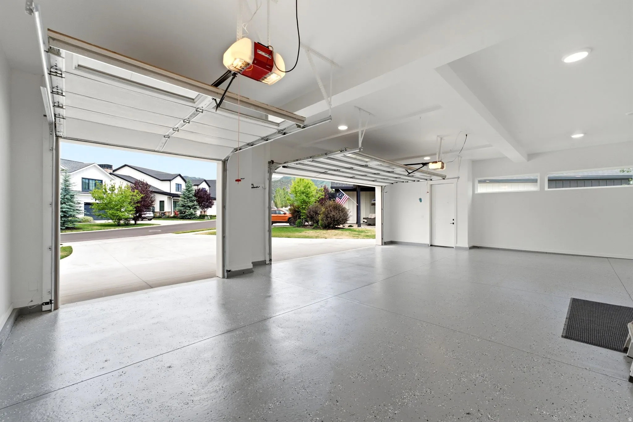 Spacious two-car garage featuring a speckled epoxy floor, white walls, recessed lighting, and high ceilings