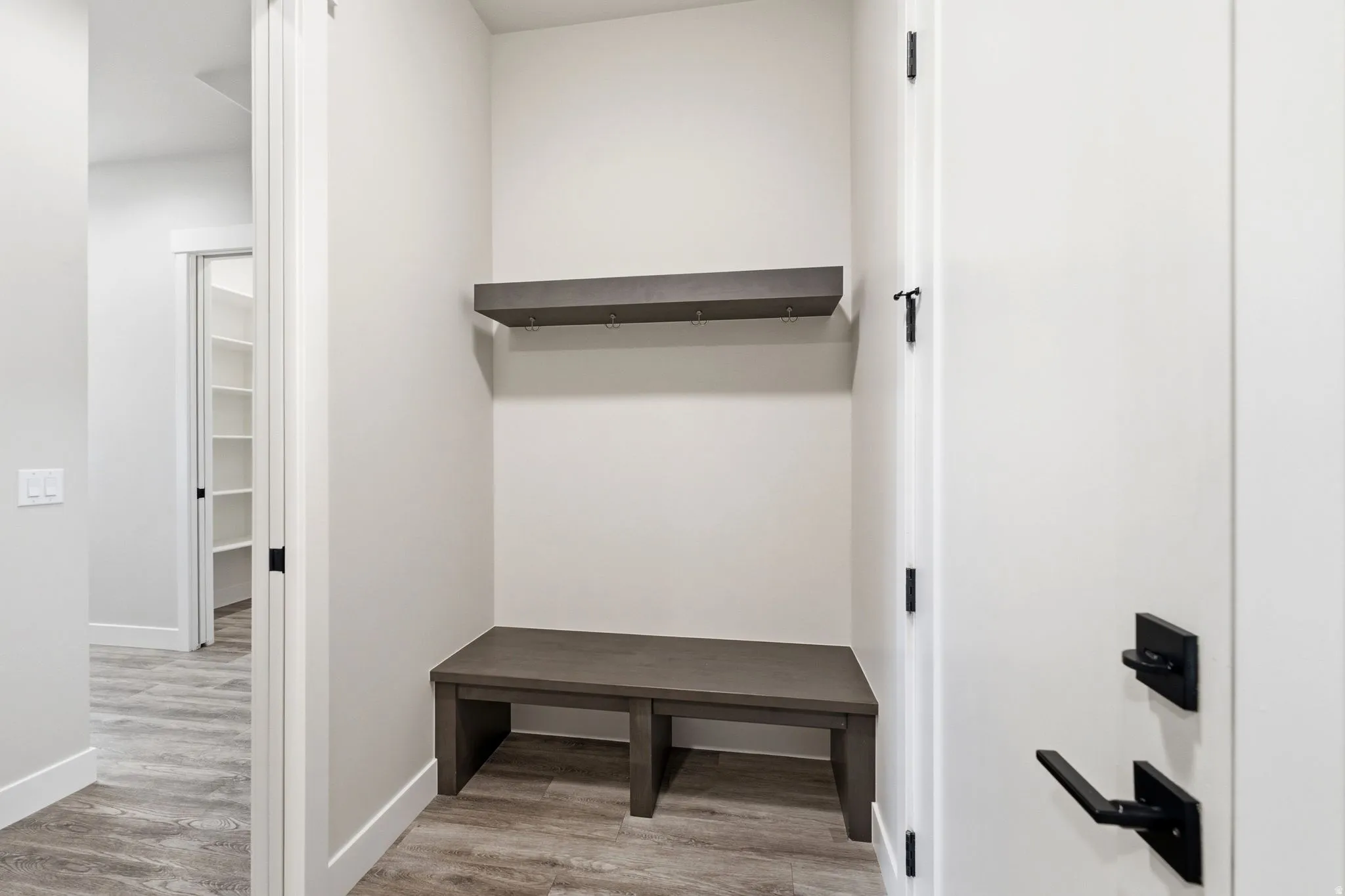 Entryway mudroom featuring a built-in bench, integrated wall shelf with hooks, and wood-finish flooring