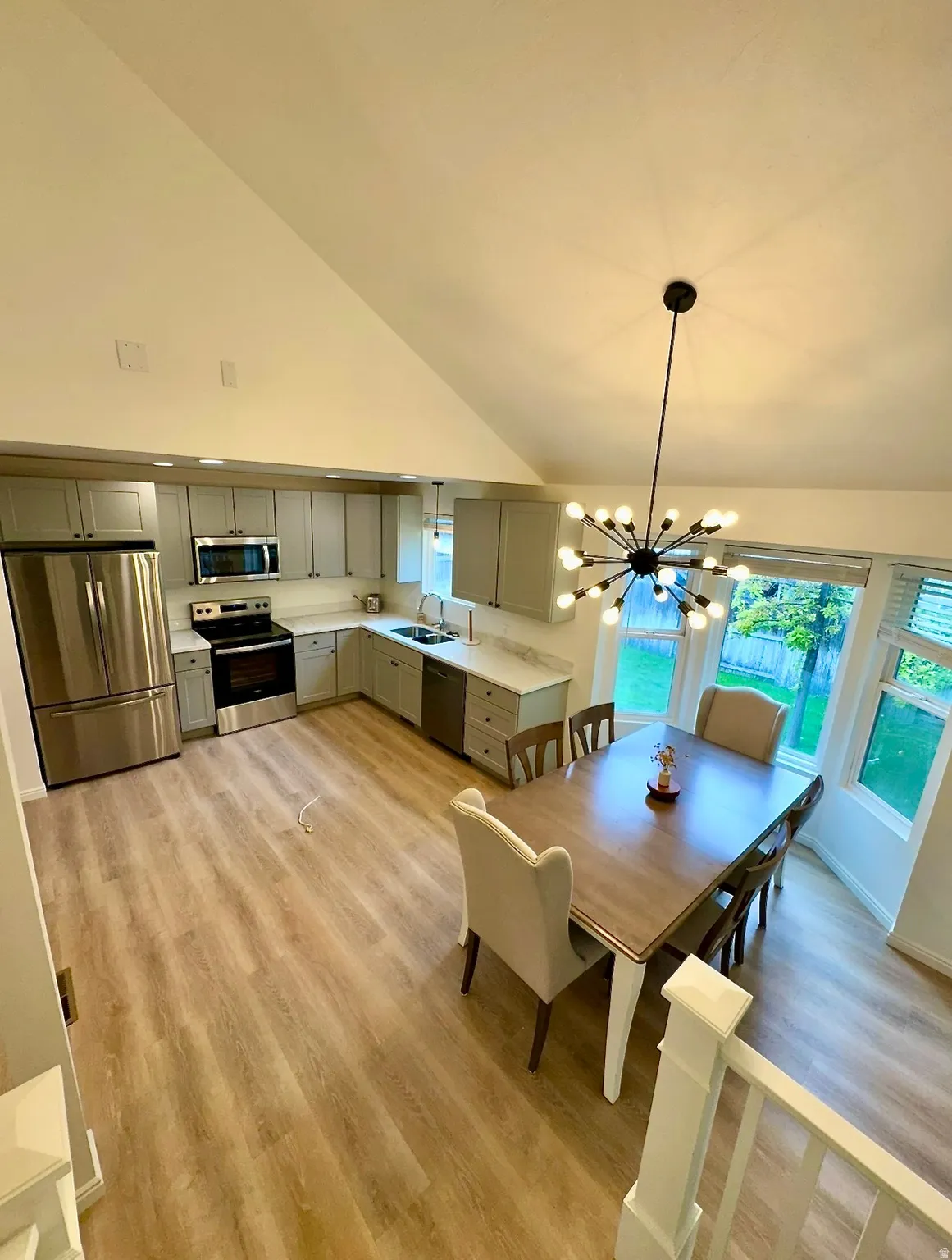 Vaulted ceiling kitchen and dining area featuring light wood-finish flooring, stainless steel appliances, and a modern sputnik chandelier