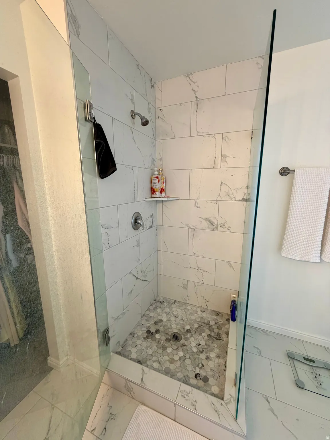 Walk-in shower with clear glass enclosure and marble-look tile walls