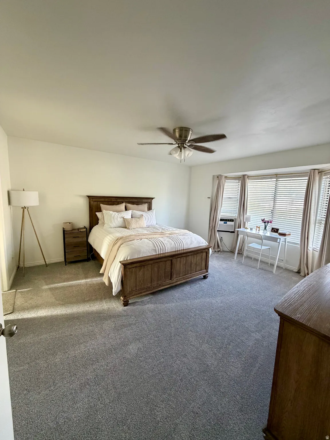 Spacious room featuring gray carpeting, a bay window with horizontal blinds, and a ceiling fan with integrated lighting