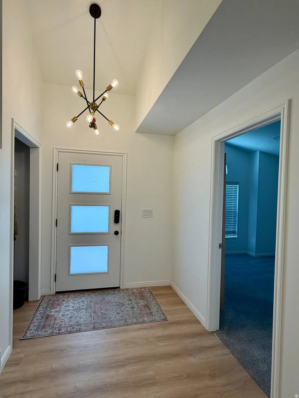 Vaulted entry featuring a modern sputnik chandelier, wood-finish flooring, and a white entry door with three rectangular frosted glass panels
