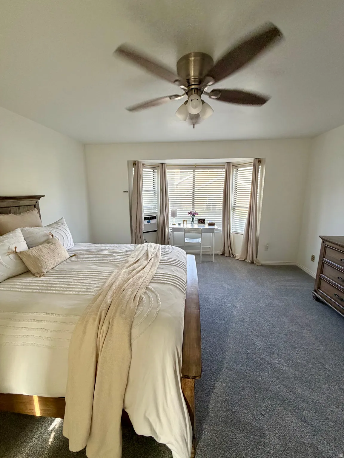 Spacious bedroom featuring a bay window, ceiling fan, neutral wall color, and gray carpeting