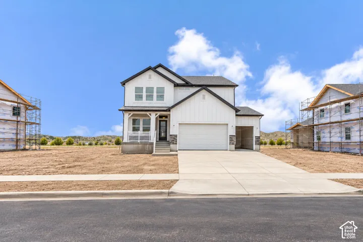 Two-story exterior featuring board-and-batten siding, stone veneer accents, a covered front porch, and a two-car garage
