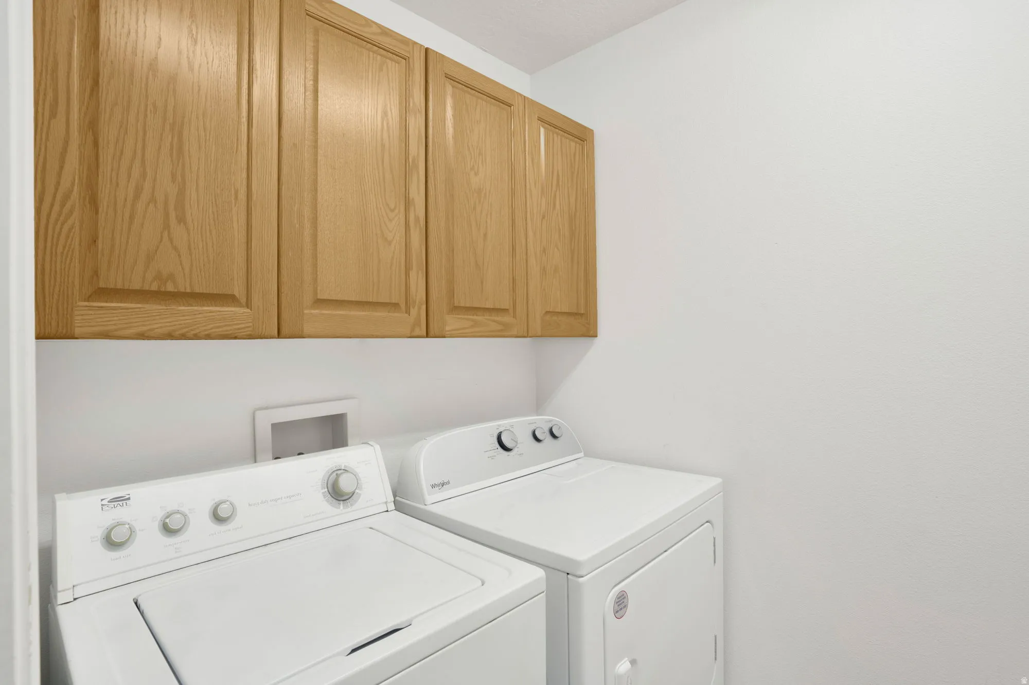 Laundry area featuring upper cabinetry with wood-finish doors, white walls, and a dedicated appliance space
