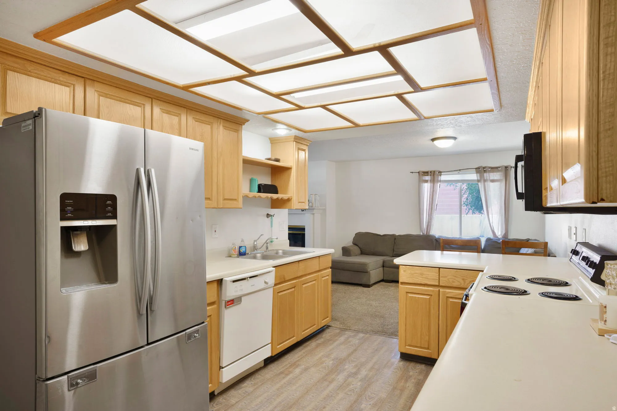 Kitchen featuring light wood cabinetry, a stainless steel French door refrigerator, white countertops, and wood-finish flooring