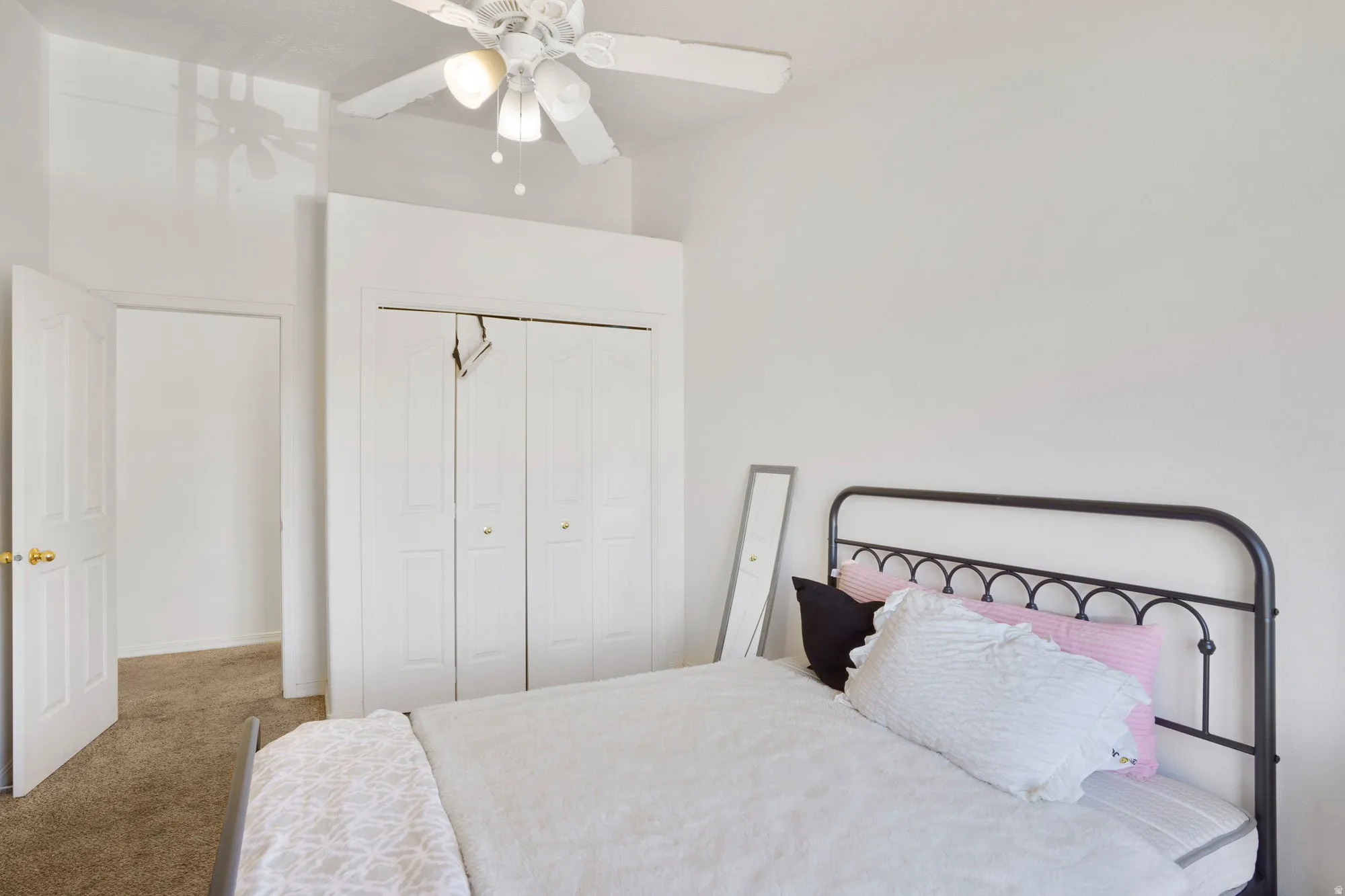 Carpeted room featuring a ceiling fan with integrated lighting, white bi-fold closet doors, and a white interior door with a brass-finish knob