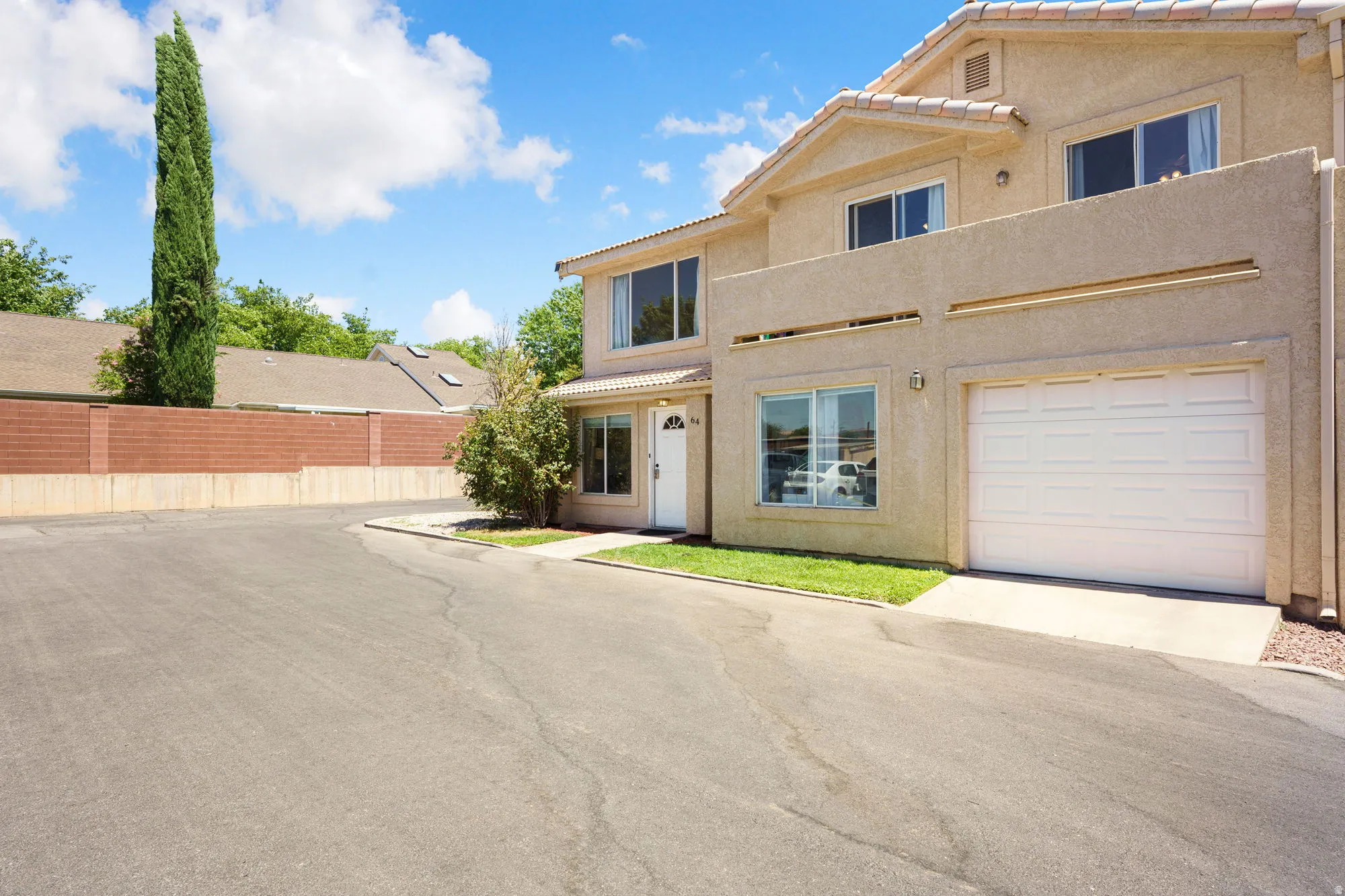 Two-story stucco exterior featuring a two-car garage with a white panel door, multiple windows, and a paved driveway