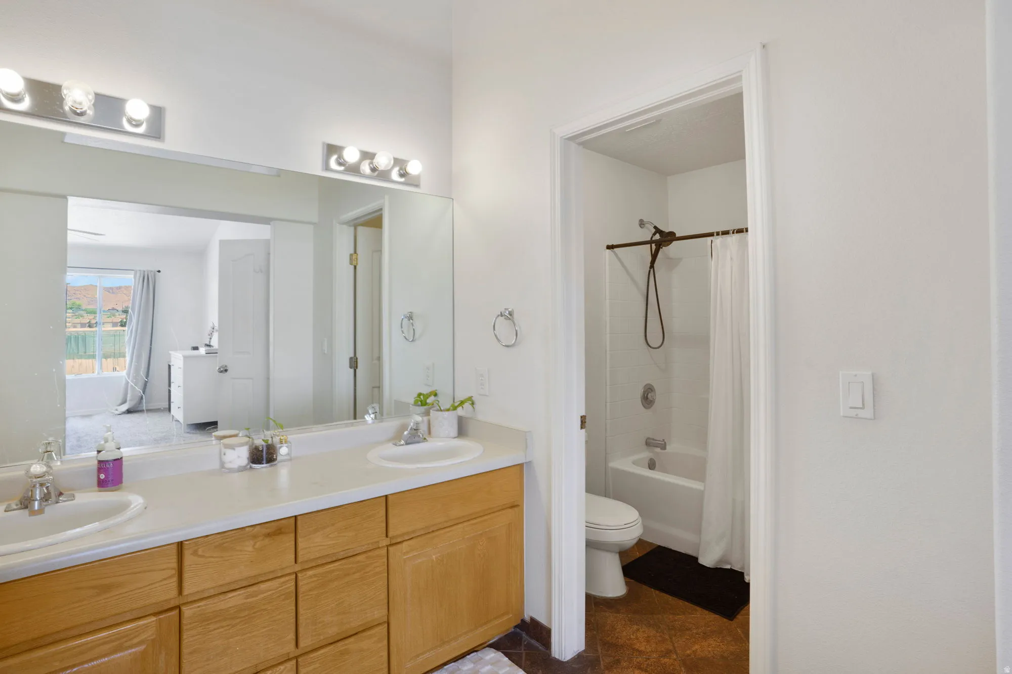 Double vanity with light wood-finish cabinetry, white countertops, and dual basin sinks