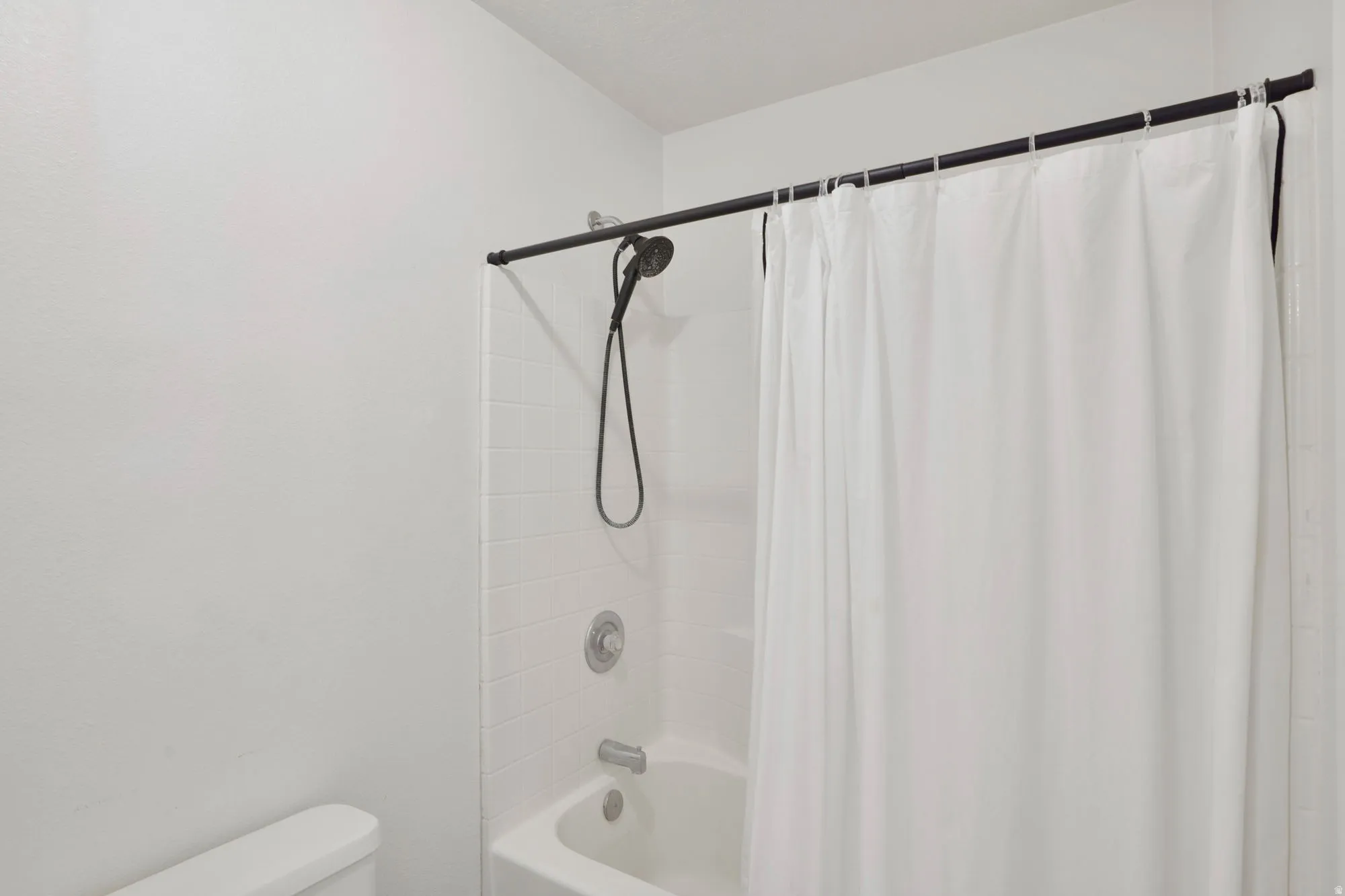 Shower-over-tub combination with white subway tile surround, matte black shower head, and coordinating shower rod
