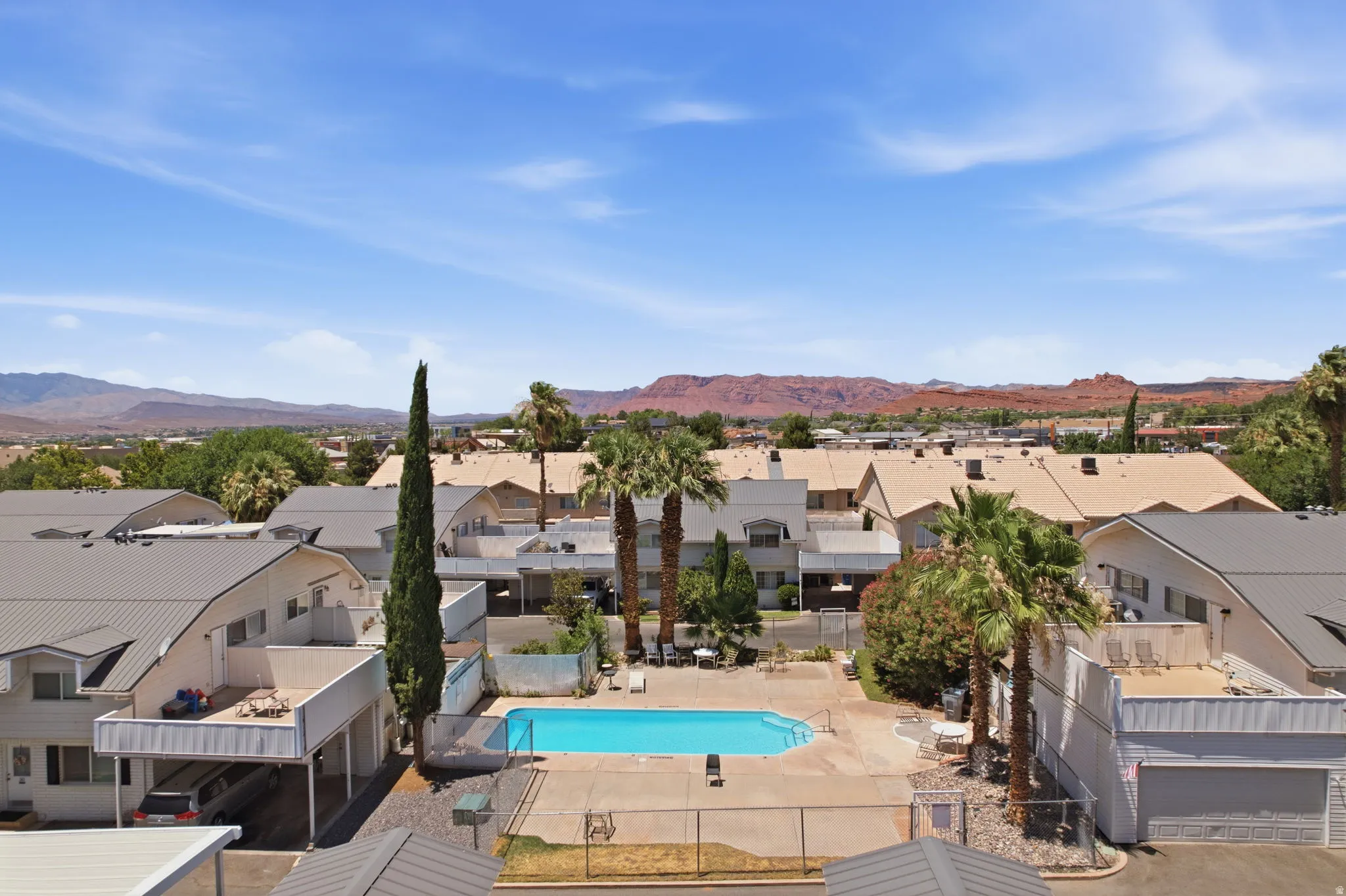 Central swimming pool with surrounding concrete decking, fenced perimeter, and nearby palm trees