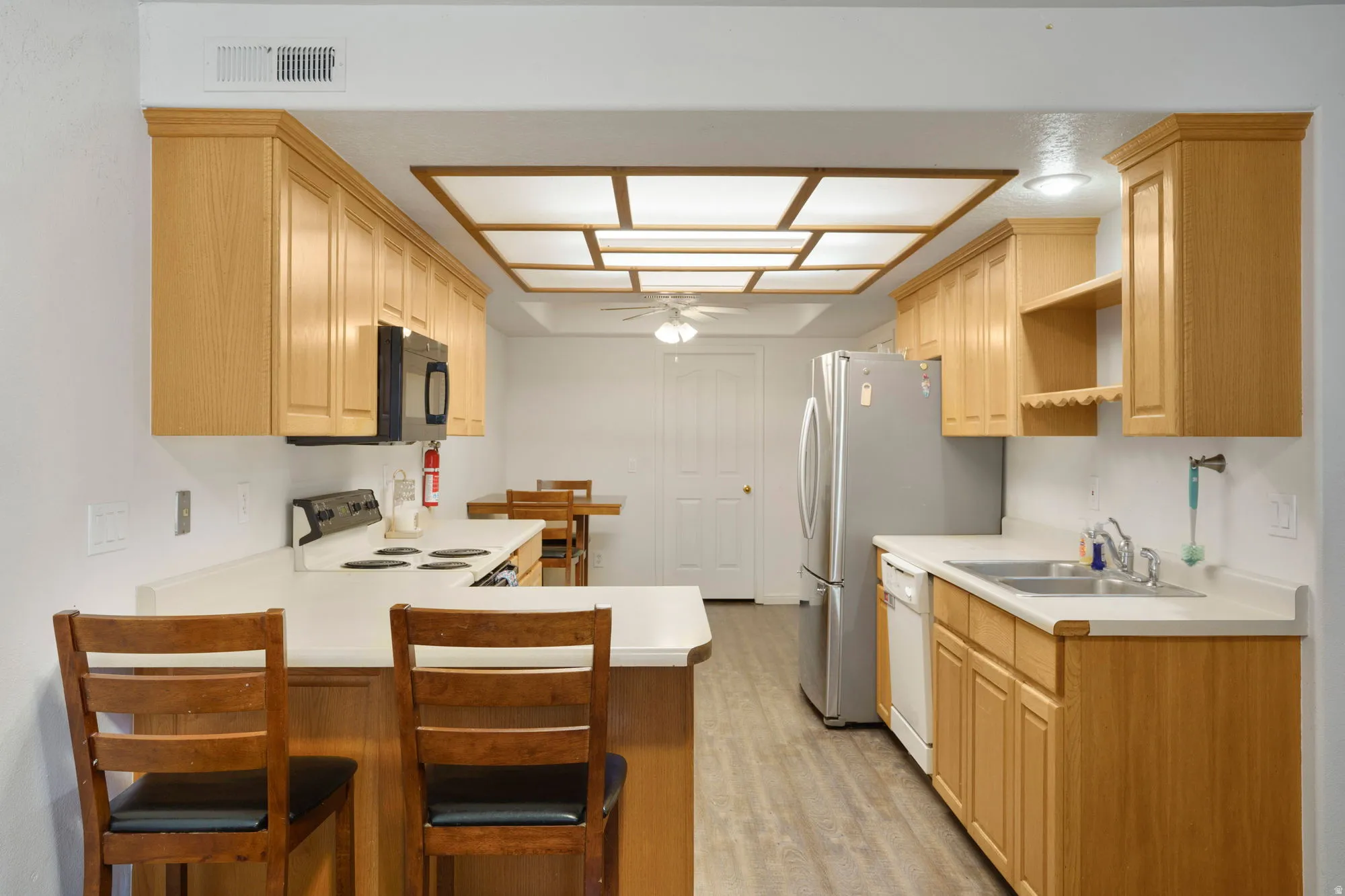Galley-style kitchen featuring wood-finish cabinetry, light countertops, wood-finish flooring, a stainless steel refrigerator, and a built-in microwave