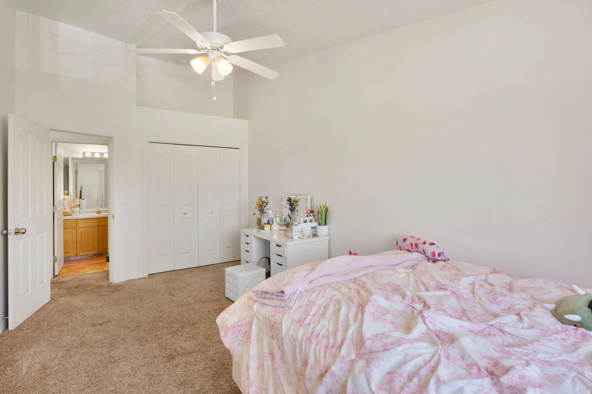 Carpeted room featuring a vaulted ceiling with a ceiling fan, bi-fold closet doors, and access to a bathroom with a vanity and mirror