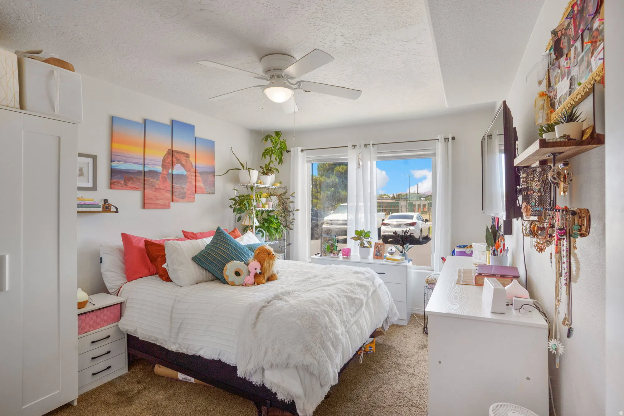Carpeted bedroom featuring white walls, a ceiling fan with integrated lighting, and a large window with white curtain rods