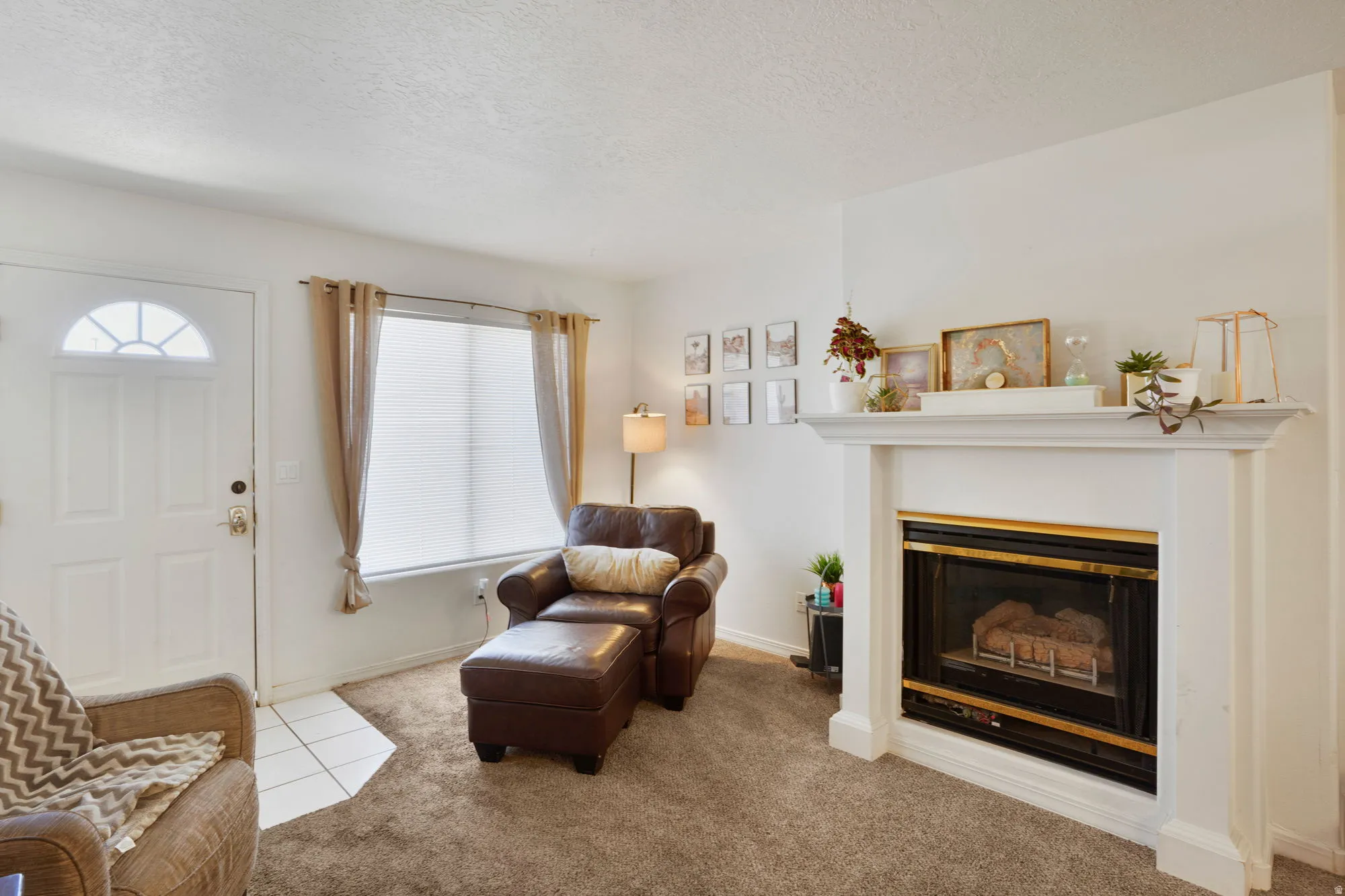 Living area featuring a white paneled entry door with a decorative transom, a large window with privacy blinds, and a white fireplace with a mantel