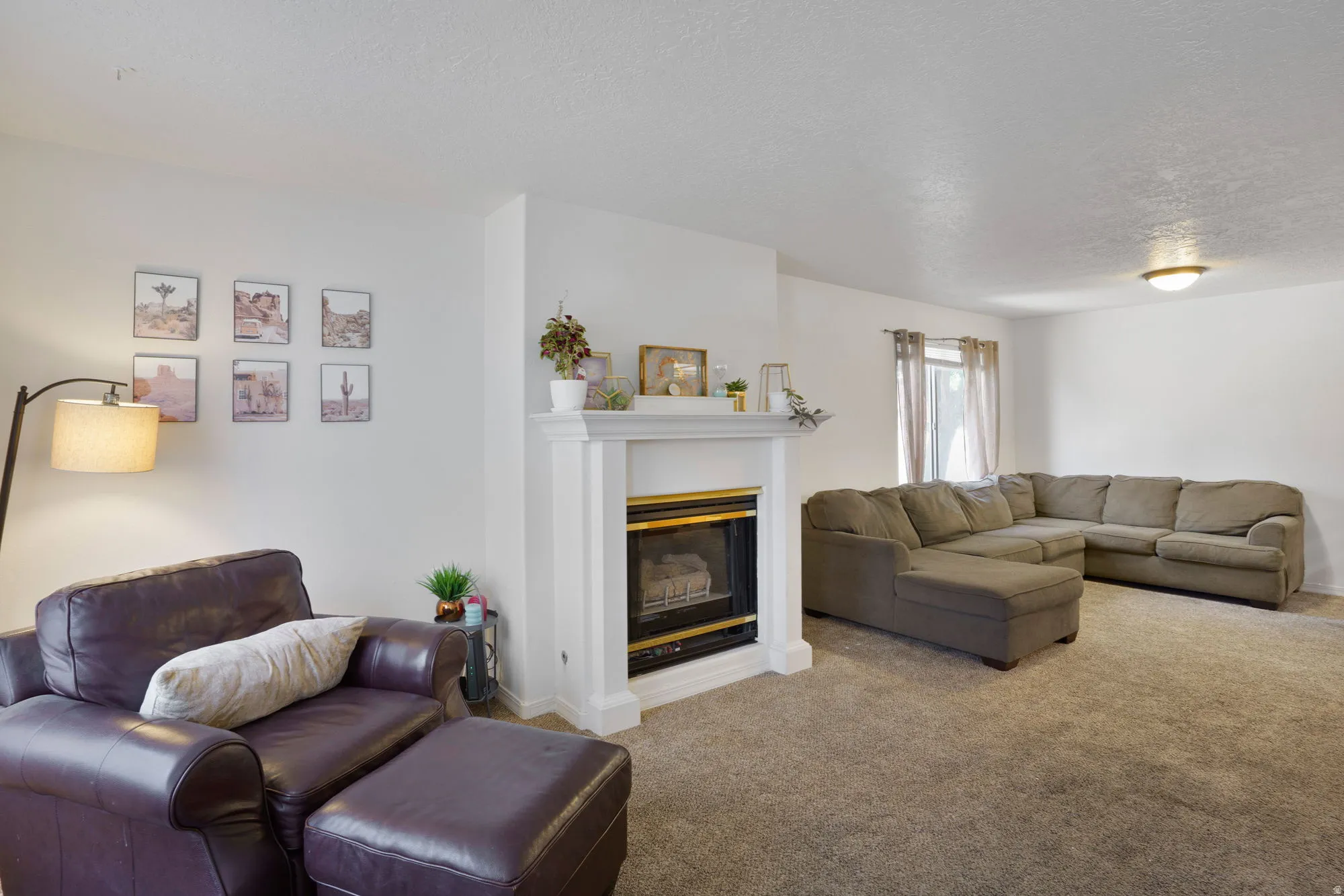 Living area featuring a white mantel fireplace with a gold-trimmed insert, light neutral carpeting, white walls, and a window with natural light