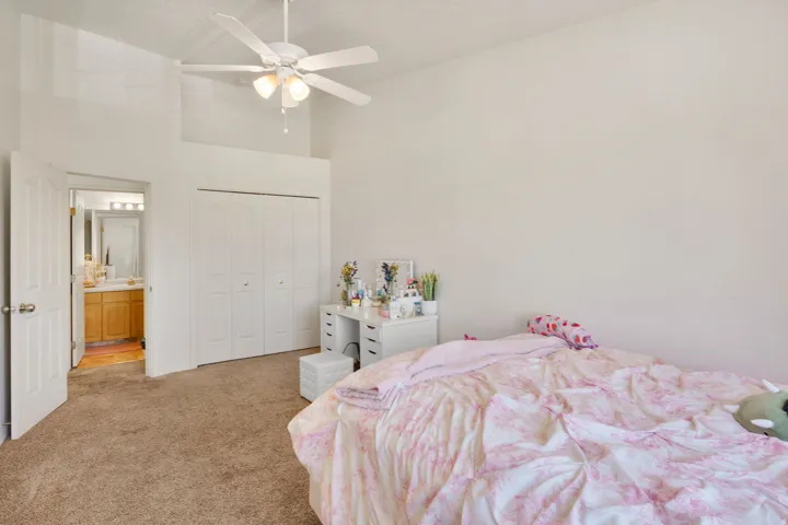 Carpeted room featuring a vaulted ceiling with a ceiling fan, bi-fold closet doors, and access to a bathroom with a vanity and mirror