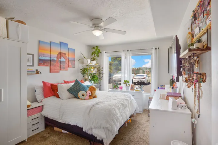 Carpeted bedroom featuring white walls, a ceiling fan with integrated lighting, and a large window with white curtain rods