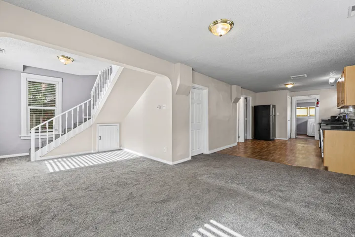 Spacious interior featuring grey carpeting, white staircase with balusters, and an under-stair storage door