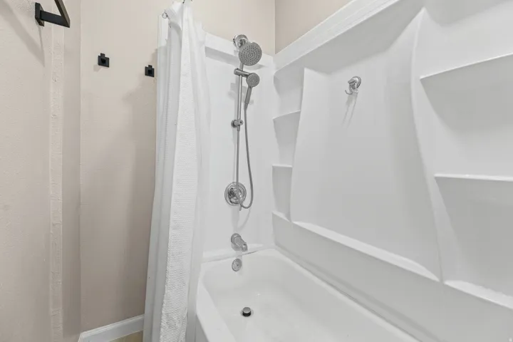 Bathtub and shower combination featuring a white surround with integrated shelving and a chrome shower head with handheld sprayer