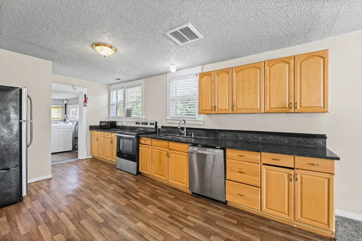 Kitchen featuring wood-finish flooring, light wood cabinetry, dark countertops, and a stainless steel dishwasher