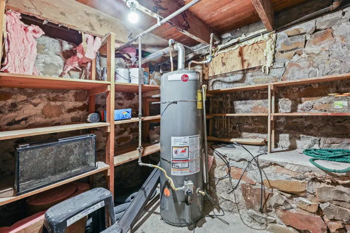 Utility space featuring a water heater, exposed stone walls, and extensive wooden shelving