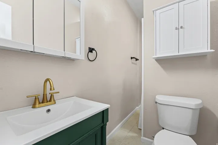 Bathroom featuring a green vanity with white integrated sink, gold-finish faucet, and coordinating wall-mounted storage cabinets