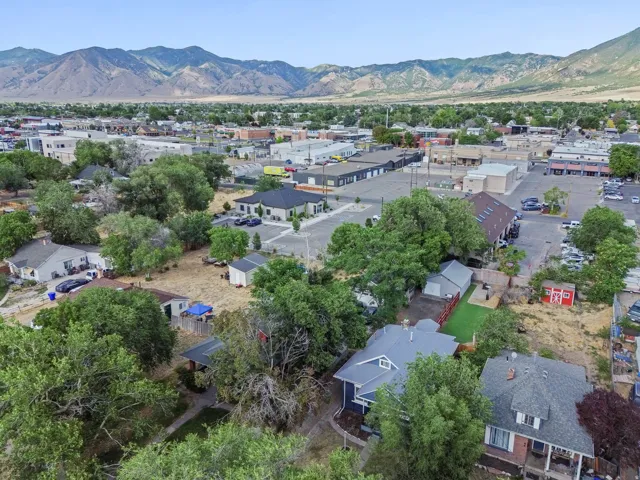 Expansive aerial perspective showcasing a residential area with mature trees, commercial buildings, and mountain scenery