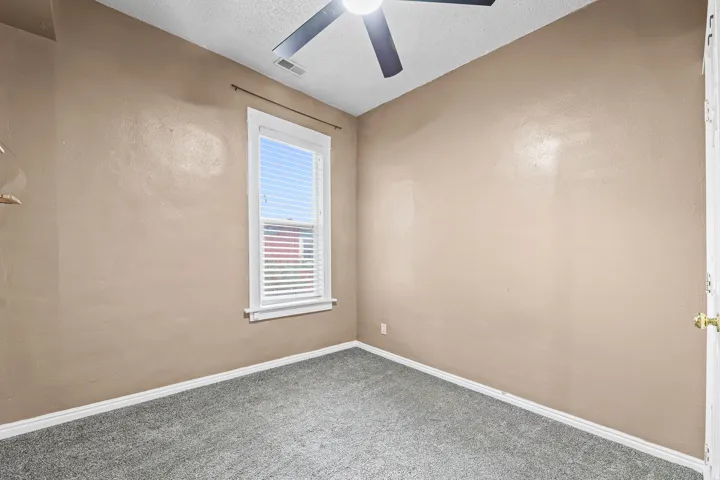 Neutral-toned interior room with gray textured carpeting, a white-framed window with horizontal blinds, and a ceiling fan with integrated lighting