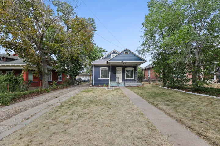 Blue exterior with white trim, covered front porch, concrete walkway, and mature trees