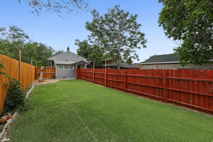 Expansive backyard featuring a lush green lawn, full privacy fencing, and a mature tree