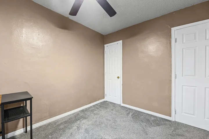 Room featuring textured walls with neutral paint, two paneled doors with gold-toned hardware, gray carpeting, white baseboards, and a ceiling fan