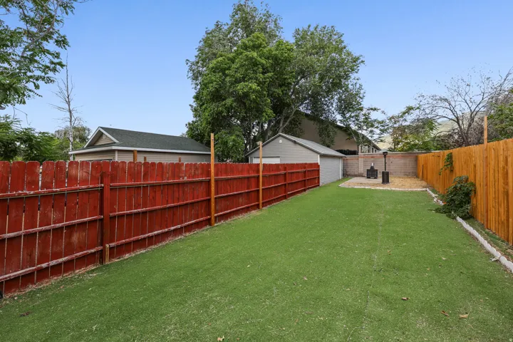 Expansive backyard featuring artificial turf, a red-stained wood fence, and a natural wood fence